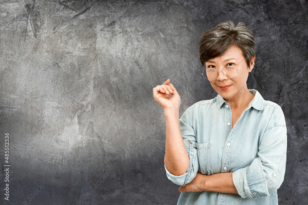 Photo of beautiful old Asian woman with gray hair, wearing glasses and blue shirt, standing on dark gray concrete wall background. Copy space backdrop, artwork. Elegant happy elderly retire concept Photo of beautiful old Asian woman with gray hair, wearing glasses and blue shirt, standing on dark gray concrete wall background. Copy space backdrop, artwork. Elegant happy elderly retire concept