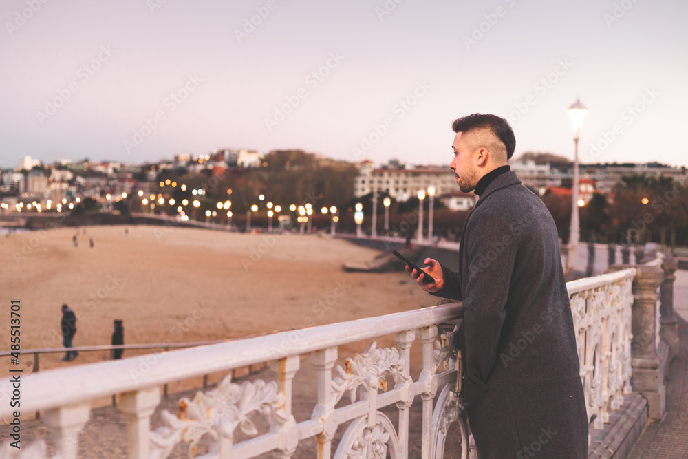 Young caucasian man using a smartphone at Donostia-San Sebastian sea walk during sunset time. Young caucasian man using a smartphone at Donostia-San Sebastian sea walk during sunset time.