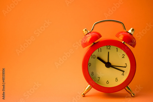 new red round clock on orange table, side view copy space