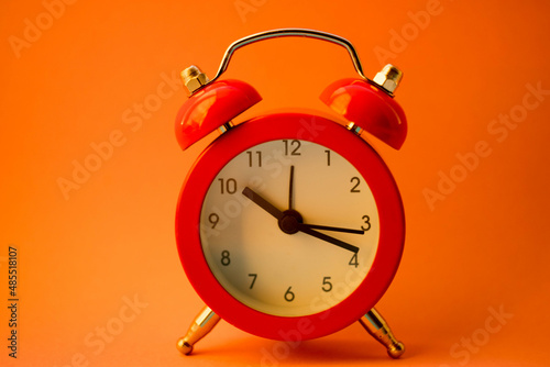 new red round clock on orange table, side view