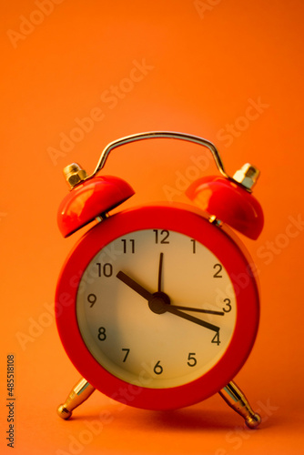 Red round clock on orange table, side view