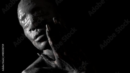 blindfolded woman is smearing clay on her skin in darkness, horror and nightmare shot