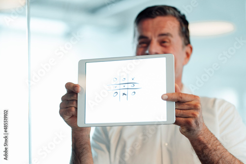 Businessman showing playing tic tac toe on screen of tablet PC at office photo