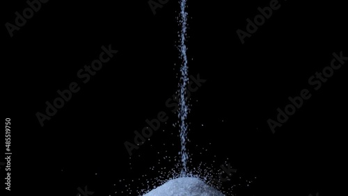 Particles of white dry sand are pouring down forming a hill on an isolated black background with blue backlight. Close up shot of crumbling natural sand grains. A stream of white sand. photo