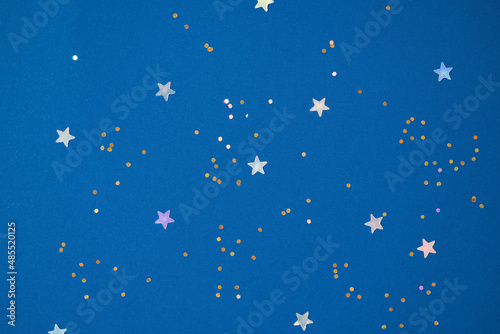 Festive background with holographic sparkling stars confetti on dark blue background. Christmas, New Year or birthday party background for your project