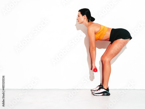 Fitness confident woman in black sports clothing. Sexy young beautiful model with perfect body. Female isolated on white wall in studio. Stretching out before training. Doing exercises with dumbbells
