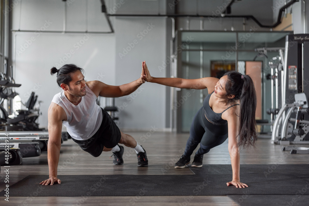 Asian woman and asian man exercise in fitness. Healthy couple doing abs exercise together in gym.