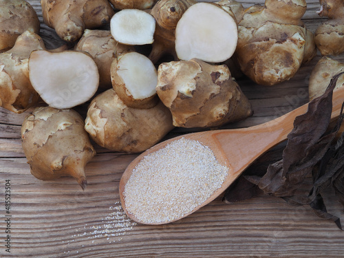 Fruits of the Jerusalem artichoke plant and natural powder with inulin on wooden table,closeup. Healthy helianthus tuberosus root vegetables and dietary supplement for diabetes 