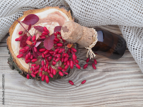 Valokuva Berries and leaves of the useful berberis plant and berberis cider, syrup in a bottle, napkin on a wooden table, top view, flat layout