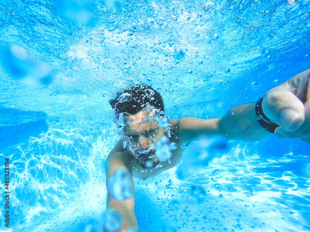 photo of a young man underwater with his arms forward having fun in the pool. there are many bubbles in the water