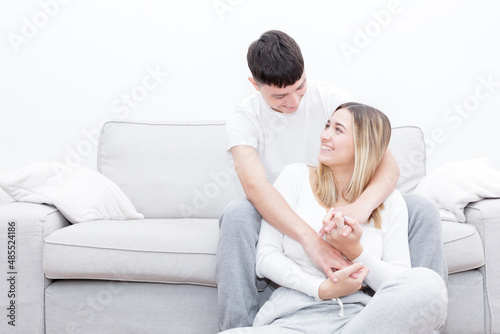 Boyfriend sitting in the sofa and girlfriend sitting between his legs looking at each other. Young couple at home. Heterosexual 18-20 years old couple.