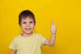 Portrait of smiling little boy with finger pointed up. Boy showing like. Kid isolated on yellow blackboard. Copy space.