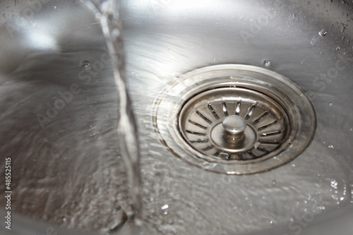 Pouring clear water stream in the kitchen metal sink closeup