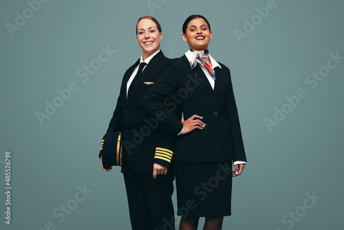 Confident pilot and flight attendant smiling at the camera in a studio