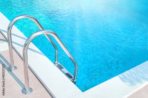 Ladder stainless handrails (stairs) into the swimming pool with blue water and sunlight (blik of sun). Vacation, relax, healthy lifestyle, sport concept.
