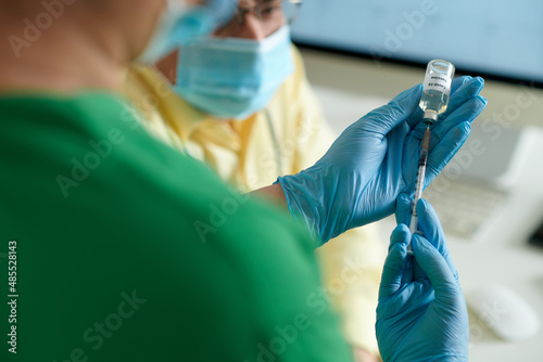 Hands of medical nurse filling syringe with vaccine against coronavirus from vial