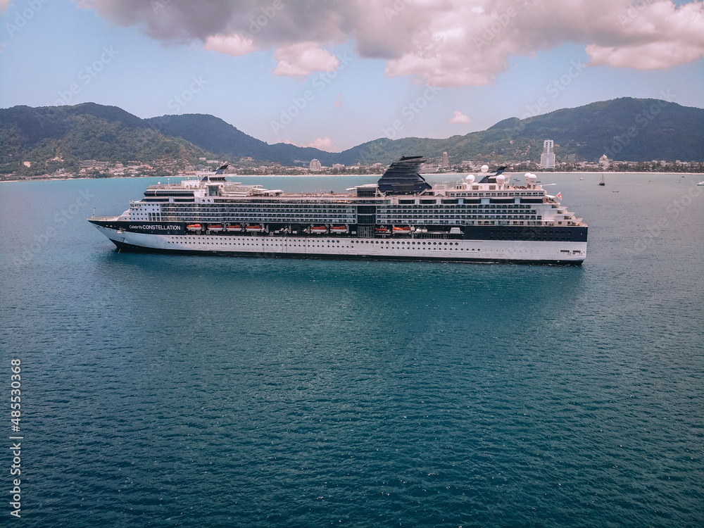 Luxurious black and white cruise liner in the harbor near the coastal European town, vast blue sea, pink clouds; drone shot, side view.
