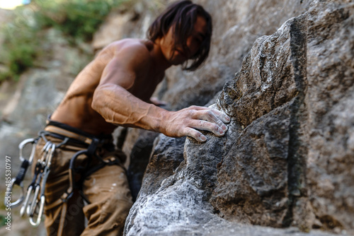 A long-haired male athlete is engaged in rock climbing on the mountain. Magnesia on the hands of a climber