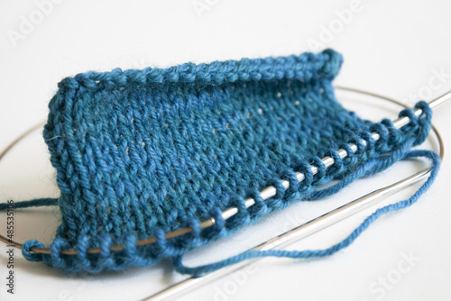 Stockinette stitch knitting on circular needles close up, blue turquoise knit stitches on white background