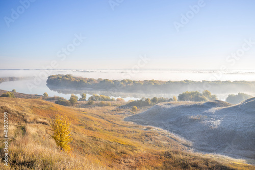 Autumn landscape in the early morning. Fog-covered expanses through which the first rays of the rising sun pass. Trees and hills in the fog. Dawn on a cold autumn morning.