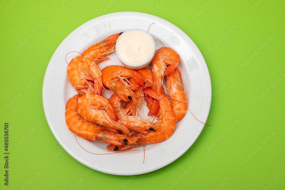 Boiled fresh shrimps with sauce in small bowl on white plate on green Boiled fresh shrimps with sauce in small bowl on white plate on green