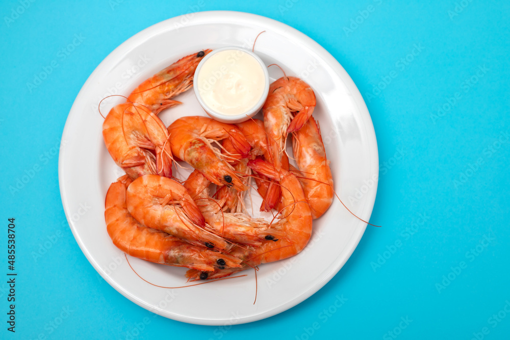 Boiled fresh shrimps with sauce in small bowl on white plate on blue Boiled fresh shrimps with sauce in small bowl on white plate on blue