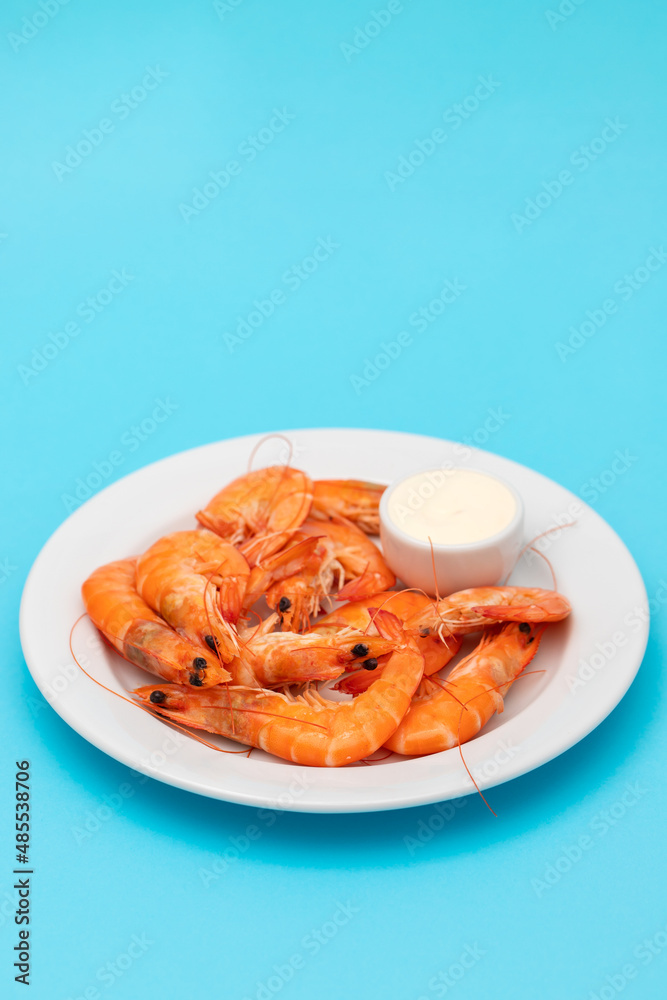 Boiled fresh shrimps with sauce in small bowl on white plate on blue Boiled fresh shrimps with sauce in small bowl on white plate on blue