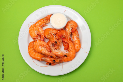 Boiled fresh shrimps with sauce in small bowl on white plate on green