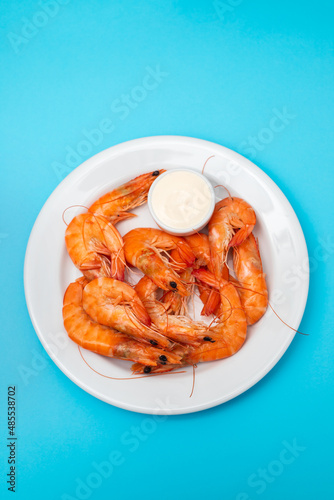 Boiled fresh shrimps with sauce in small bowl on white plate on blue