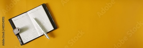 An open notebook or diary with a leather cover and a silver fountain pen lie on a yellow surface. Copy space for an inscription. Web banner photo