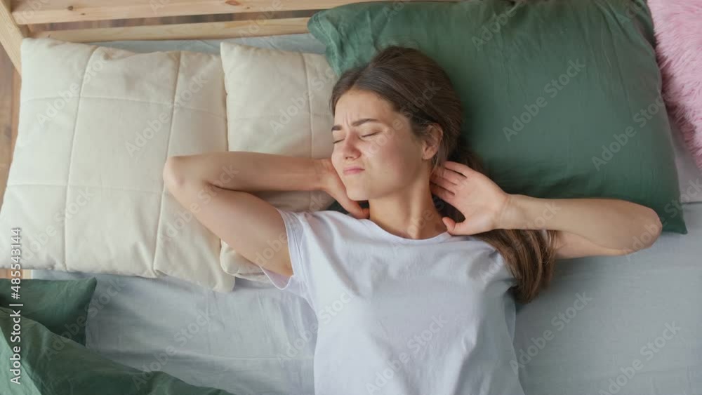 A Young Woman Wakes Up in a Bad Mood in an Uncomfortable Bed At Home, Suffers from Headaches, Insomnia. Uncomfortable Bed or Mattress, Poor Sleep, Stiffness, Pinching in the Neck. Lack of Sleep. A Young Woman Wakes Up in a Bad Mood in an Uncomfortable Bed At Home, Suffers from Headaches, Insomnia. Uncomfortable Bed or Mattress, Poor Sleep, Stiffness, Pinching in the Neck. Lack of Sleep.