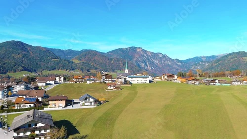 Aerial drone flyover of green field in Brandenberg village towards Church in summer with mountains in the distance at noon in Switzerland, Europe, wide view photo