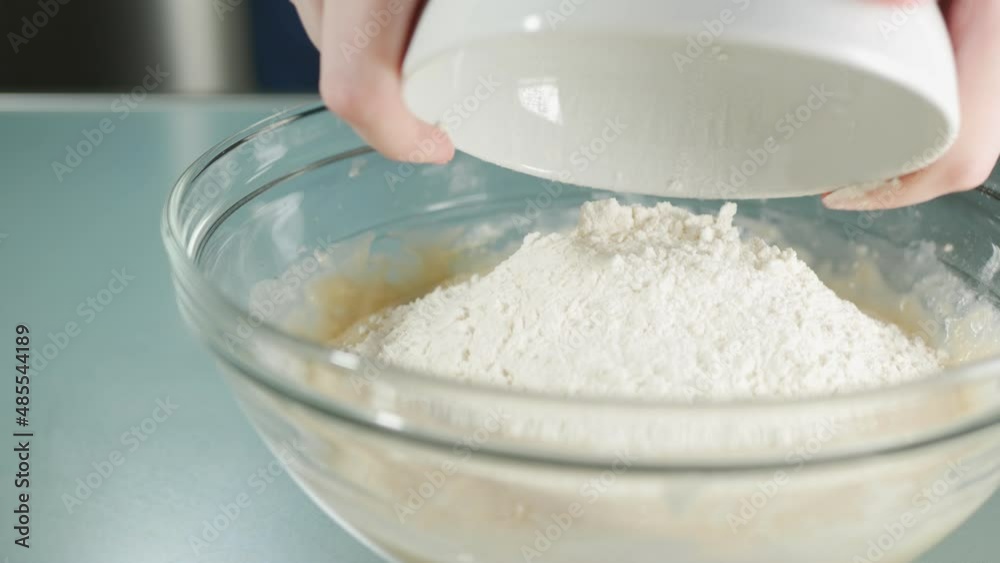 Pouring flour. into glass bowl with egg. Close-up of hands of young woman during cooking or bakery process. Isolated Pouring flour. into glass bowl with egg. Close-up of hands of young woman during cooking or bakery process. Isolated