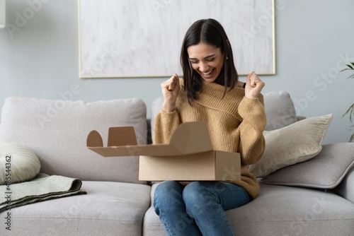 Happy young woman sit on couch room unpack cardboard box buying goods on Internet. shopping online, delivery concept photo