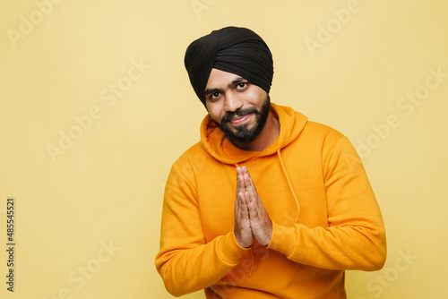 Bearded south asian man making prayer gesture while smiling