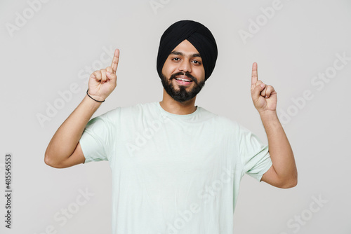 Bearded south asian man wearing turban pointing fingers upwards photo