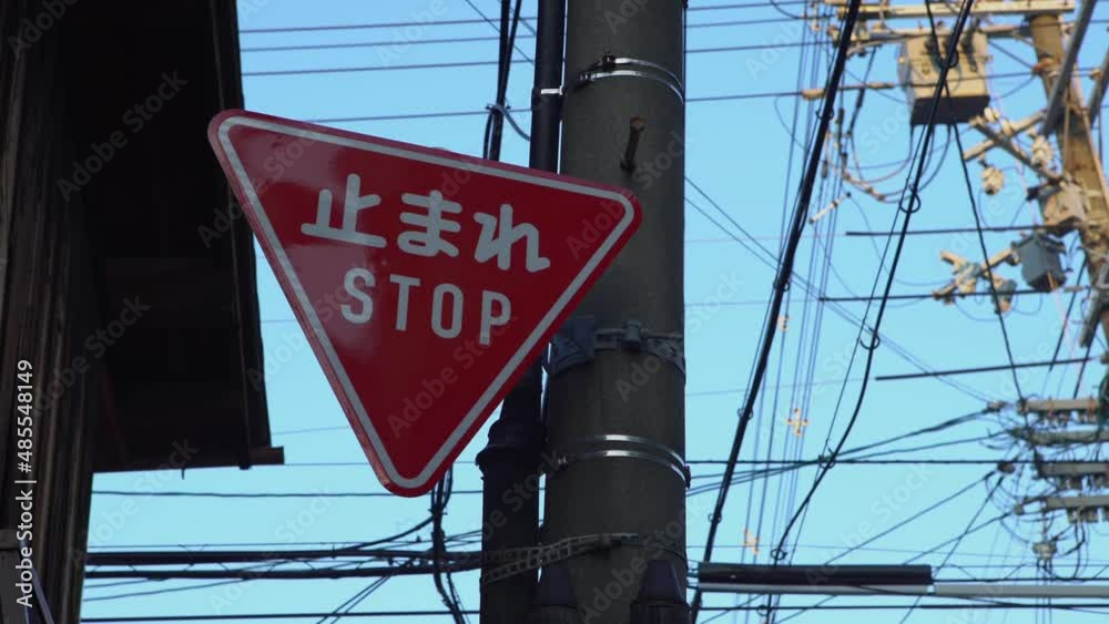 Red triangular stop warning traffic road sign with white letters kanji standing at the local street junction in Japan. Translation of the word in Japanese means stop