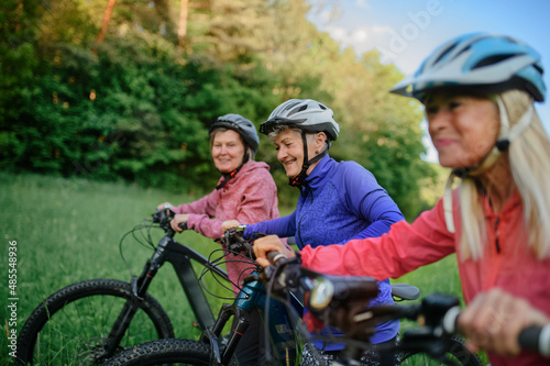 Happy active senior women friends pushing bicycles together outdoors in nature.
