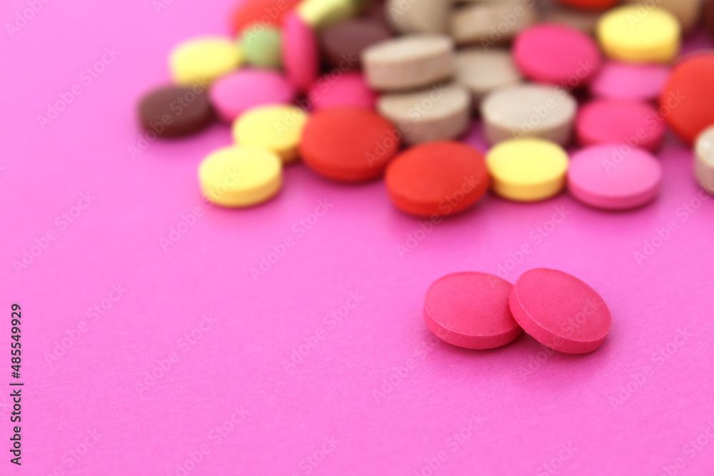 Two pink pills lie on a pink background and a bunch of different pills.