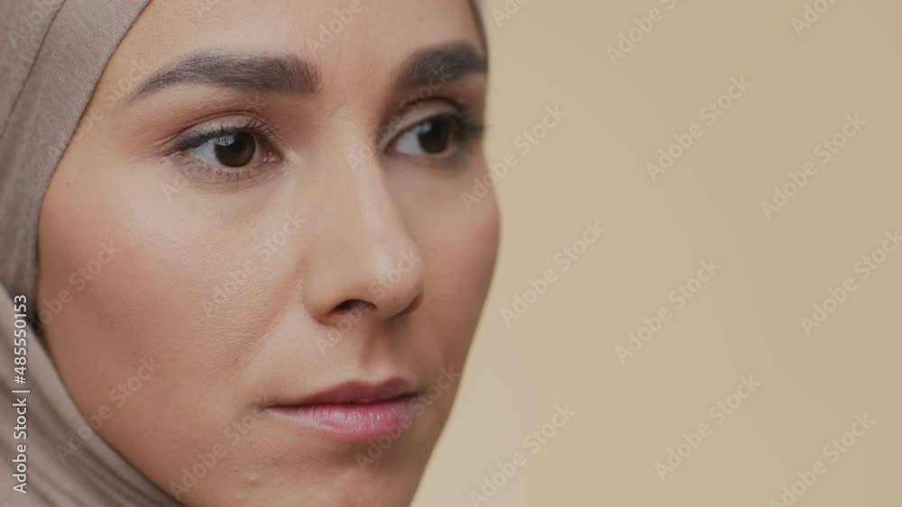 Close up portrait of young serious muslim woman in traditional headscarf looking aside, beige background, empty space Close up portrait of young serious muslim woman in traditional headscarf looking aside, beige background, empty space