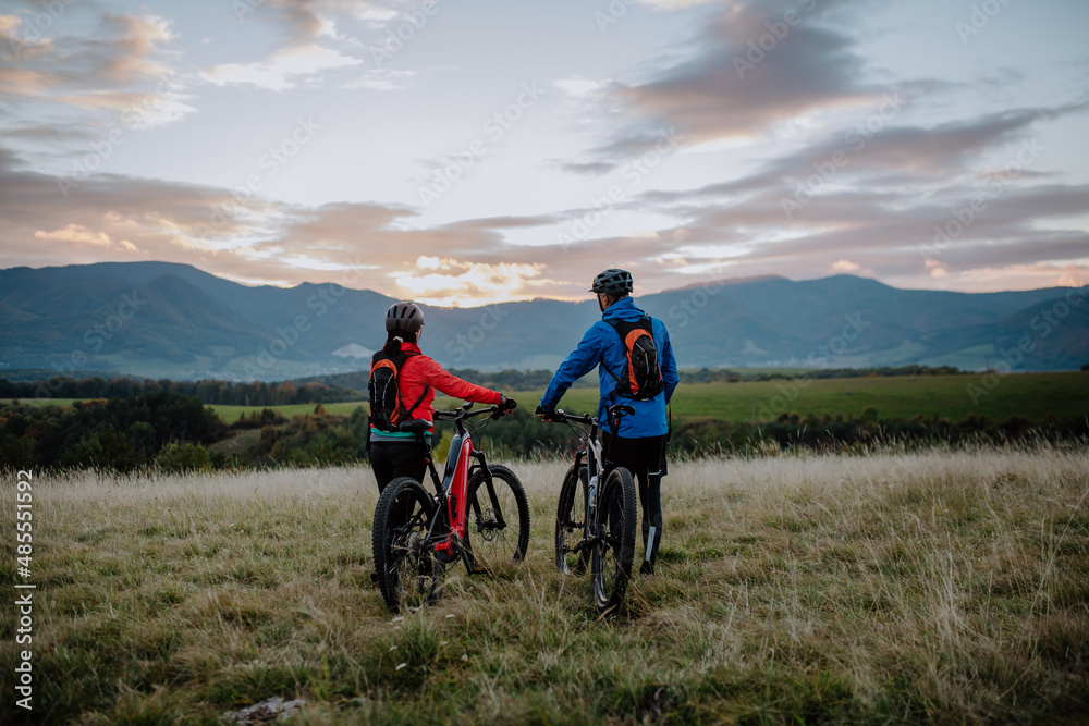 Rear view of senior couple bikers walking and pushing e-bikes outdoors in forest in autumn day. Rear view of senior couple bikers walking and pushing e-bikes outdoors in forest in autumn day.