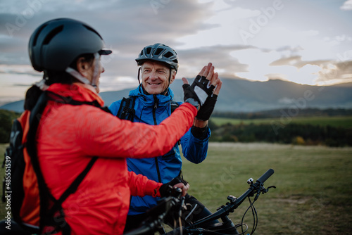 Senior couple bikers high fiving outdoors in nature in autumn day.