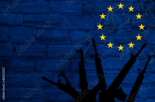 Weapons silhouettes on the background of the EU flag. Stone wall with a map of the European Union. The concept of the militarization of Europe. copy space.