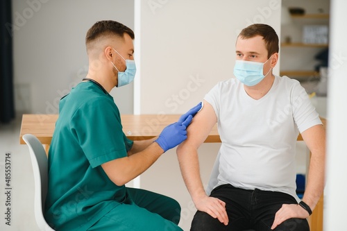 medicine  vaccination and healthcare concept - doctor wearing face protective medical mask for protection from virus disease with syringe doing injection of vaccine to male patient