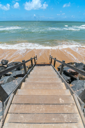 Beachfront landscape of a wooden stair leading down to the sea, beautiful blue sky day. Boa Viagem beach in Recife, PE, Brazil.