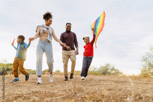 Billede på lærred Black family laughing and flying kite while running together