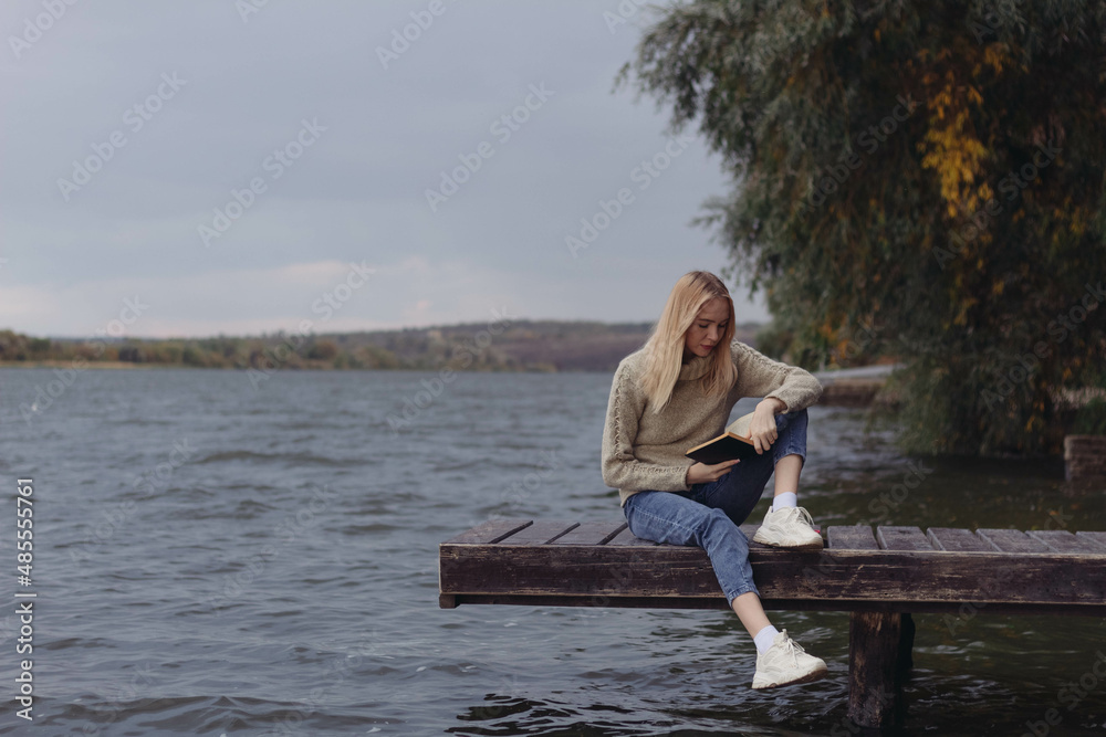 In autumn, a girl on the riverbank reads a book