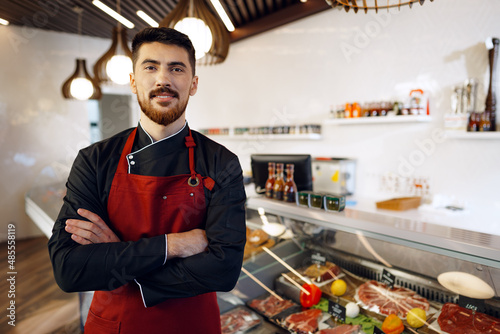 Portrait of a young man shopkeeper standing by meat stall in supermarket photo