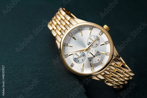 A gold wristwatch with a white dial rests on a stone table.
