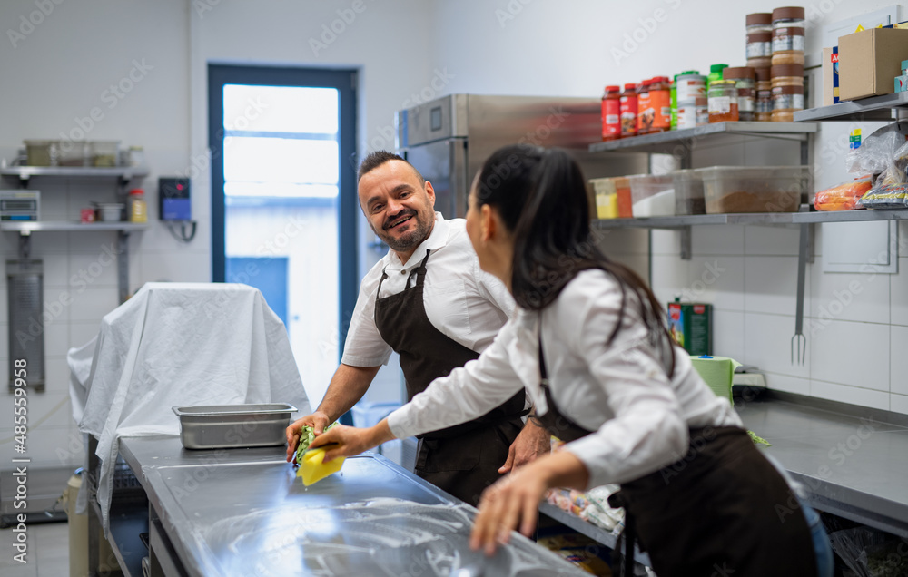 Naklejka premium Chef and cook cleaning the workspace after doing dishes indoors in restaurant kitchen.